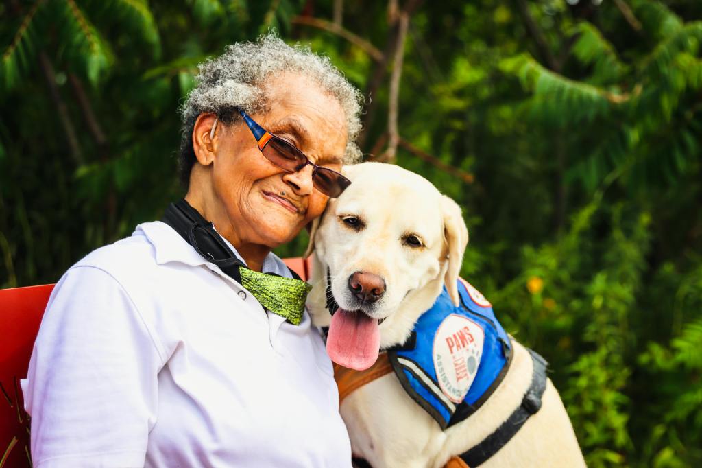 A woman leans her head against that of a therapy dog. Both look happy and relaxed.